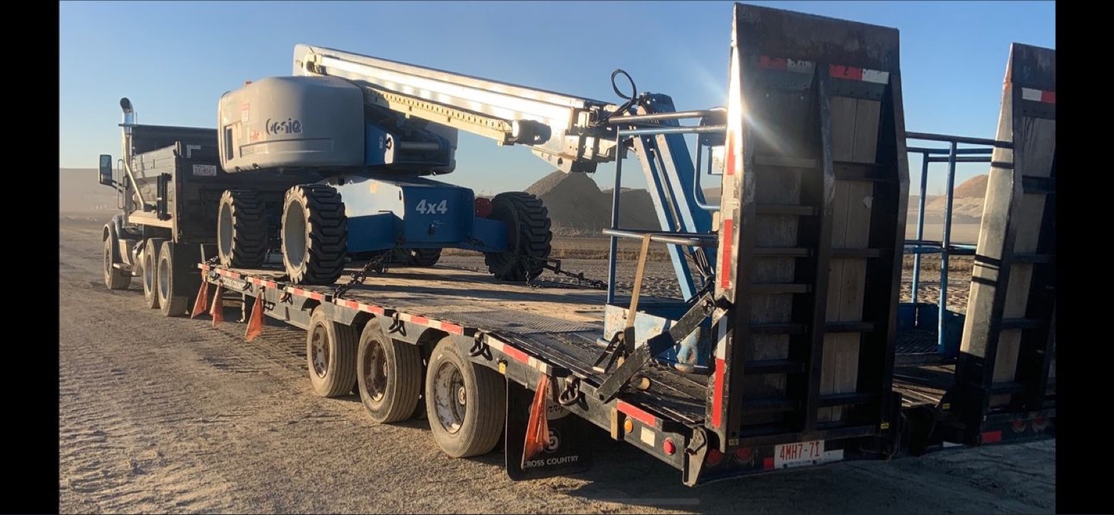 Genie boom lift on a step-deck trailer at a gravel pit