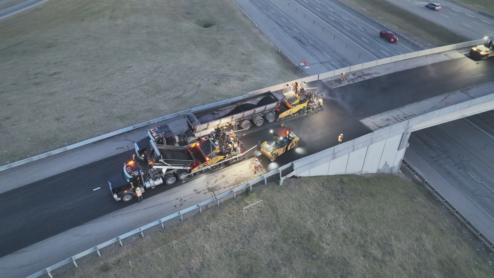 Aerial view of overpass paving with an A.F. Trucking dump truck feeding the paver