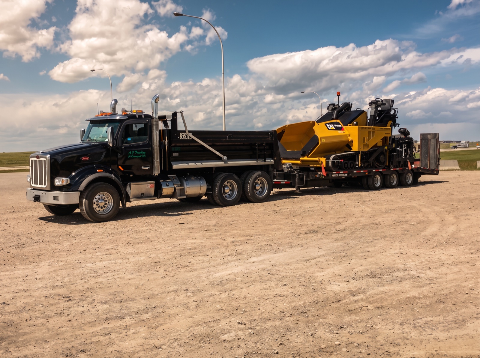 Black Peterbilt tandem dump truck pulling a step-deck trailer loaded with a CAT paver