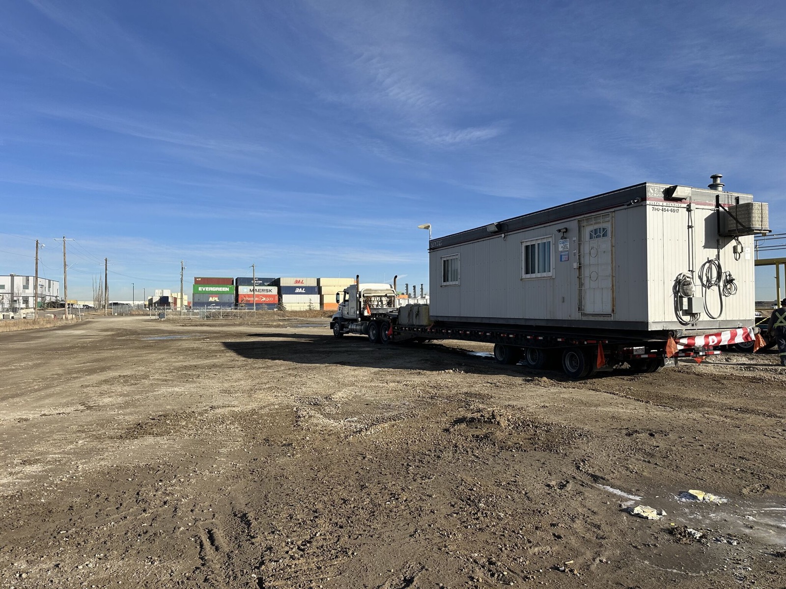 Office trailer skid shack on a step-deck trailer leaving a container yard
