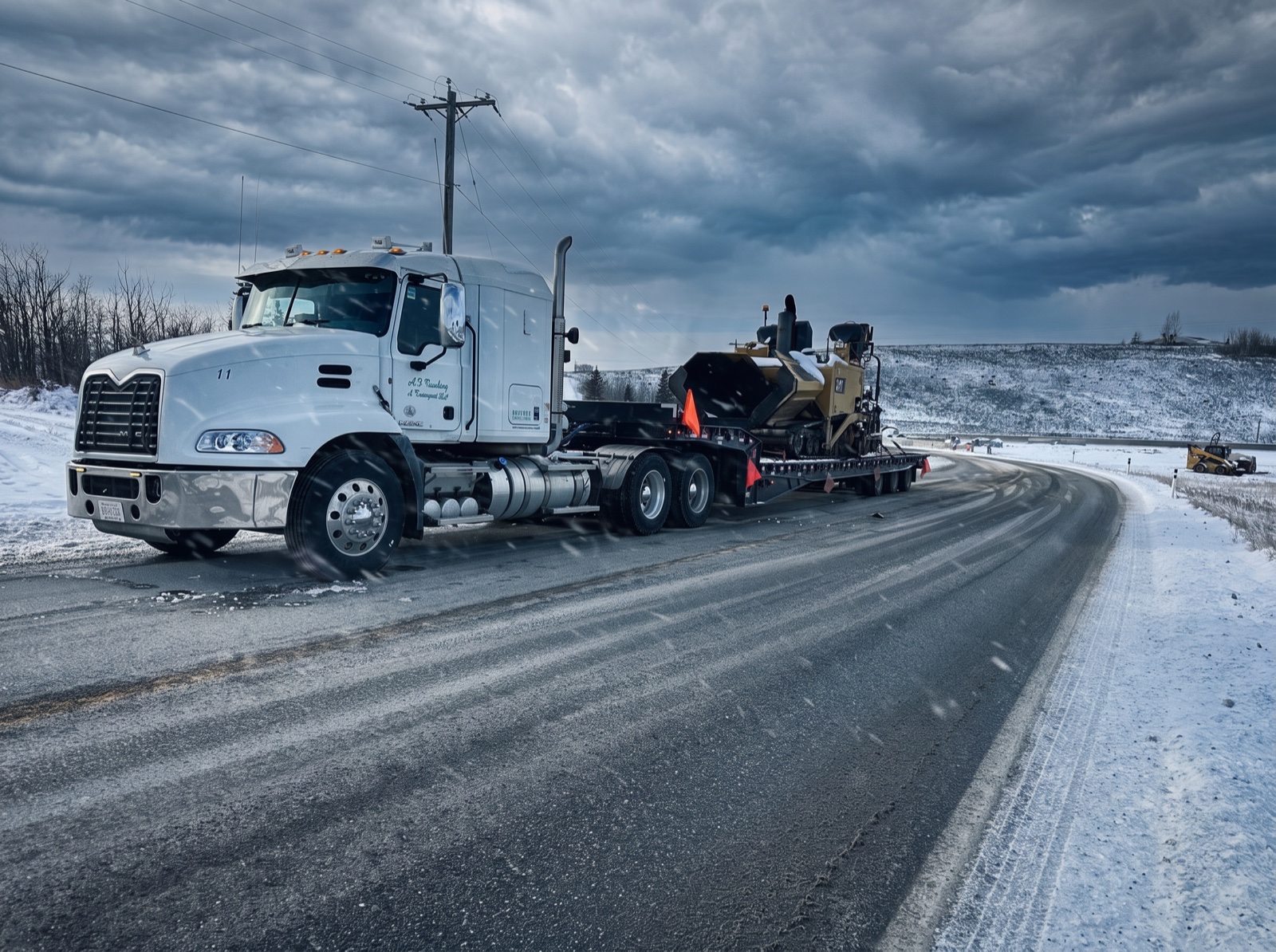White Mack highway tractor pulling a step-deck trailer with a CAT paver around an icy curve
